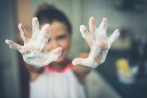  A student in a school bathroom washing their hands with soap and water, pracitcing good hand hygiene. 